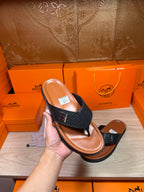Hand holding a black leather thong sandal with H logo strap and tan sole.