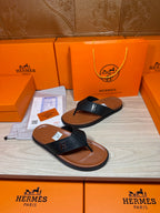 Black leather slide thong sandals with H logo strap and tan-brown sole.