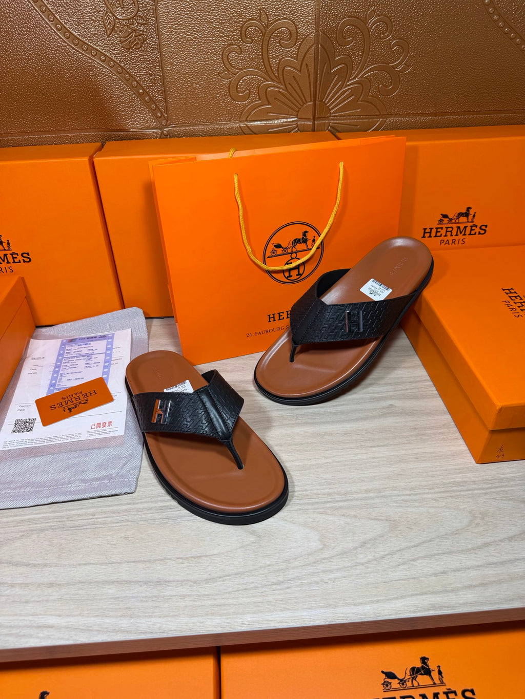 Two black leather thong sandals with H logo straps and tan-brown soles.