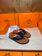 Black leather thong sandals with H logo straps and brown footbeds.