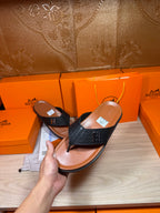 Hand-held black leather thong sandals with H logo strap over tan footbeds.
