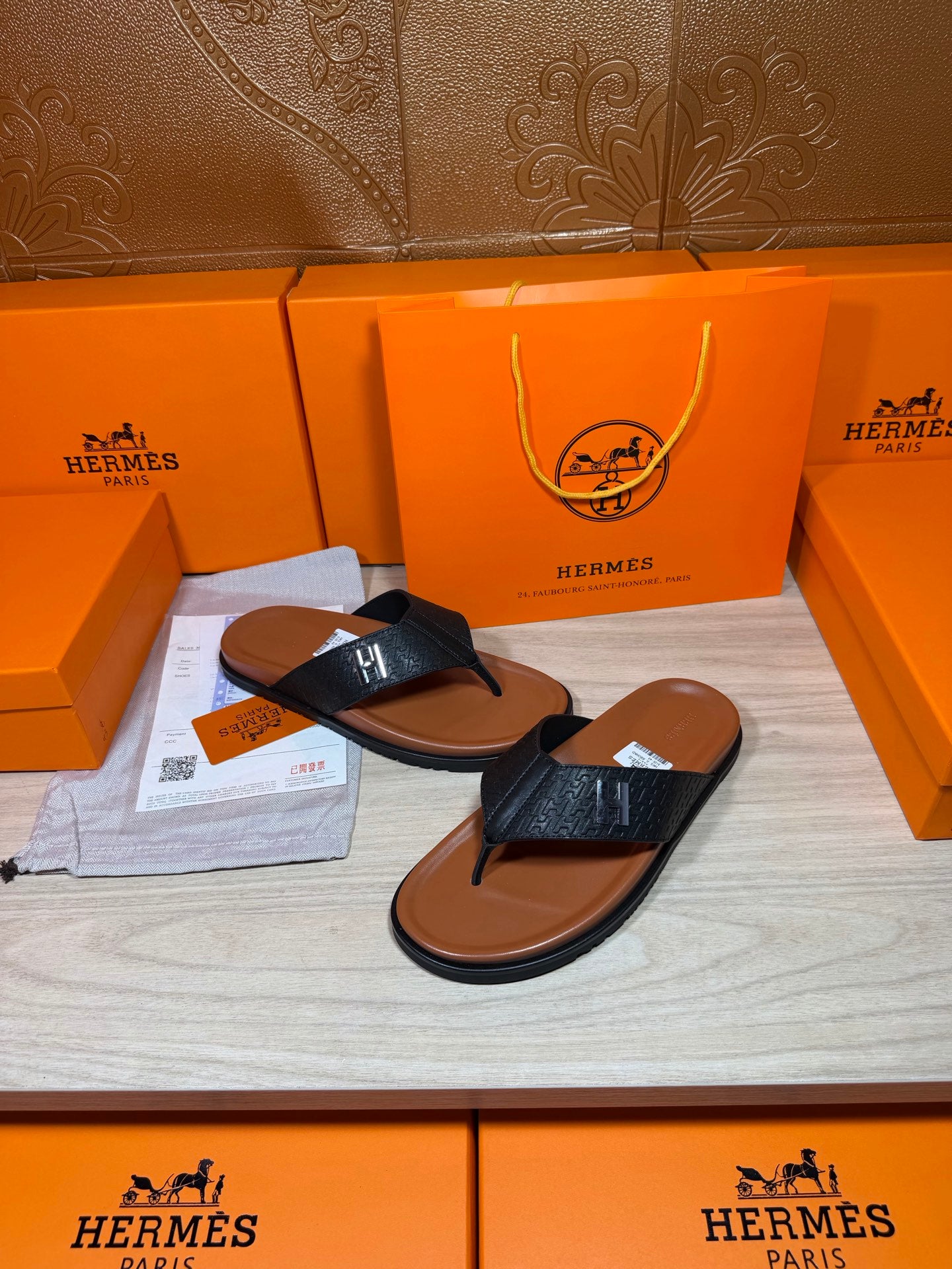 Black leather thong sandals with H logo strap and tan-brown outsole.