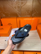 Luxury leather sandals held in hand, dark navy straps with black rubber sole