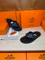 Luxury leather sandals with dark navy straps and black soles beside shoe box