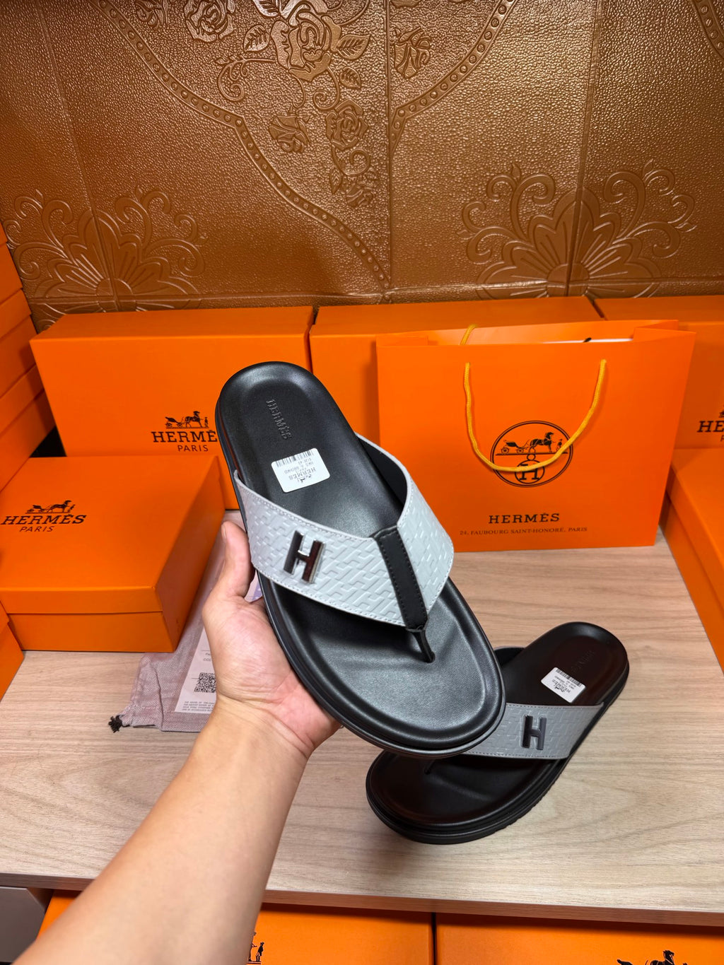 Hand holding black thong sandal with light gray strap and H logo