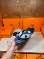Black thong sandal with light gray H strap resting on display surface
