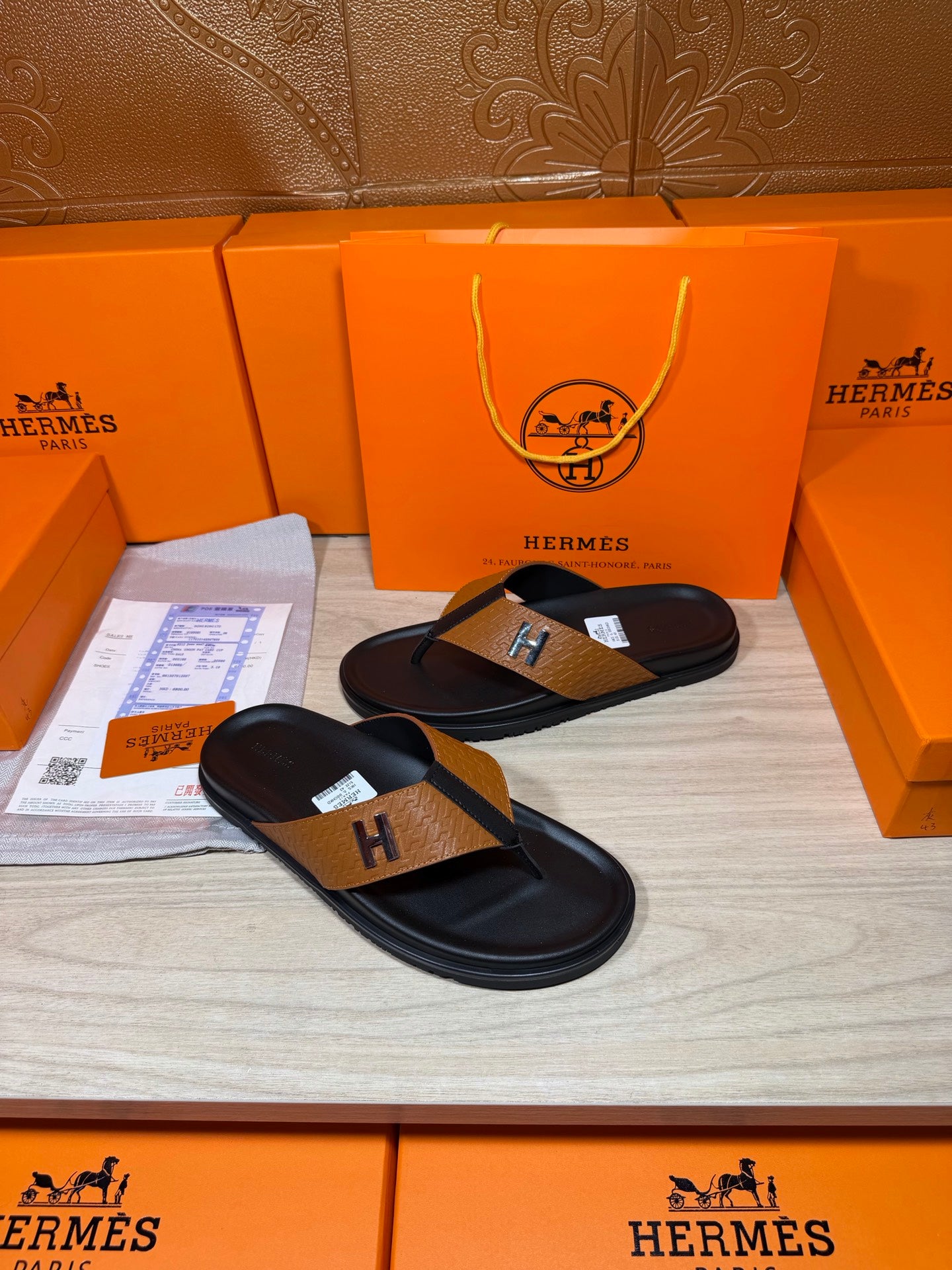 Hermes black leather thong sandals with tan strap and H logo buckle, pair on display