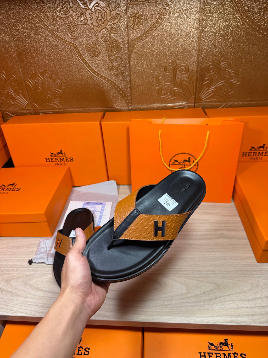Hermes black leather thong sandal held in hand, tan strap with H logo buckle