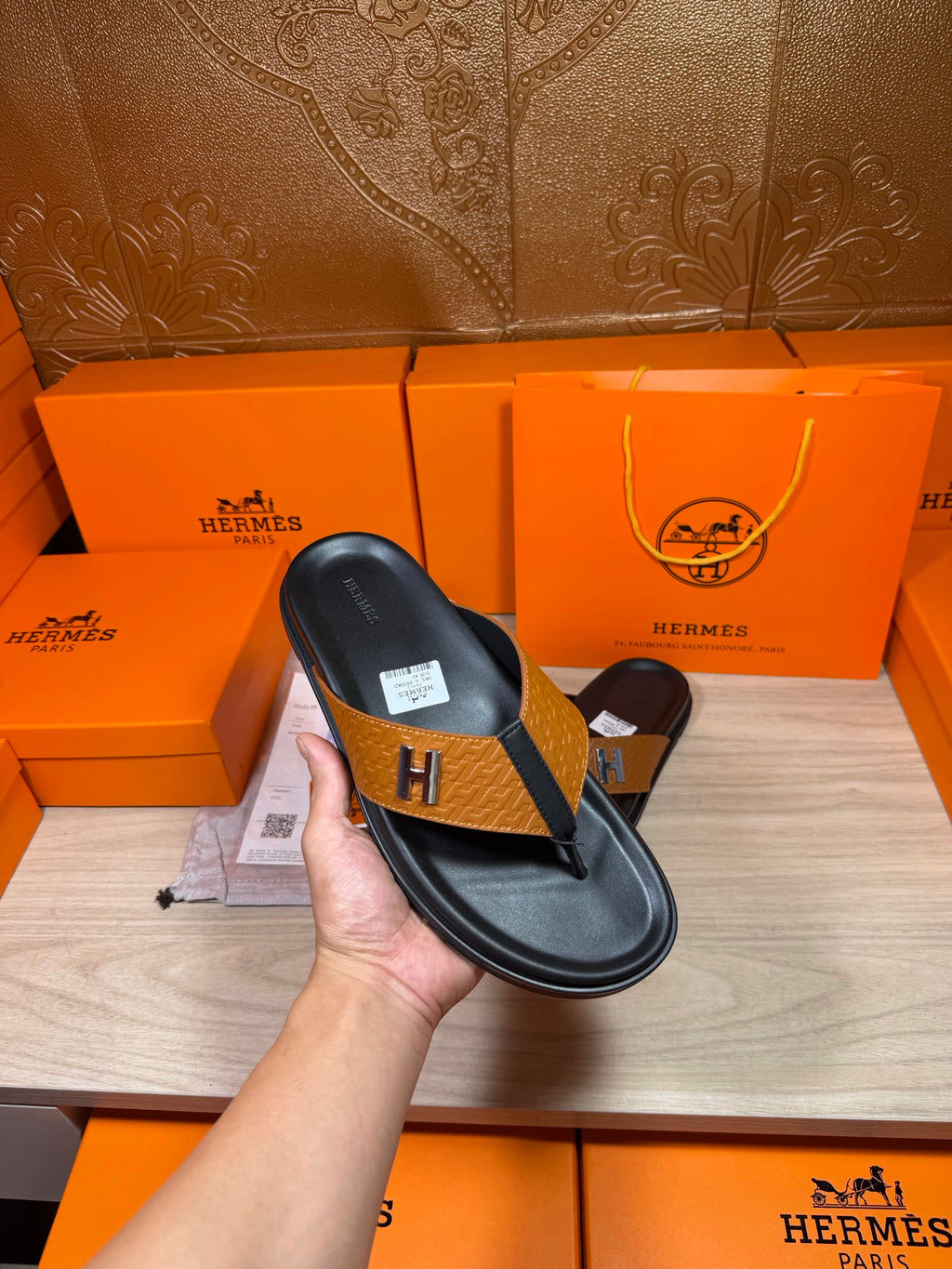 Hermes black leather thong sandal held in hand, tan strap with H logo buckle