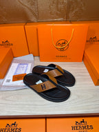 Hermes black leather thong sandals with tan strap and H logo buckle, top view