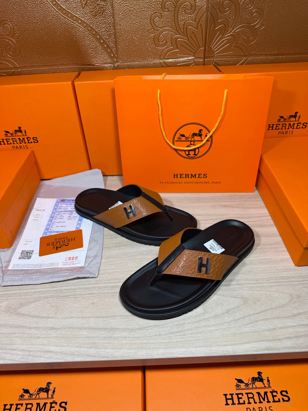 Hermes black leather thong sandals with tan strap and H logo buckle, angled pair