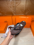 Hand holding brown leather thong sandal with dark H strap detail