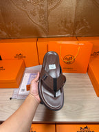 Brown leather flip-flop sandal held in hand, sole and H strap visible