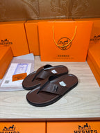 Brown leather flip-flop sandals with dark H strap detail, pair on display