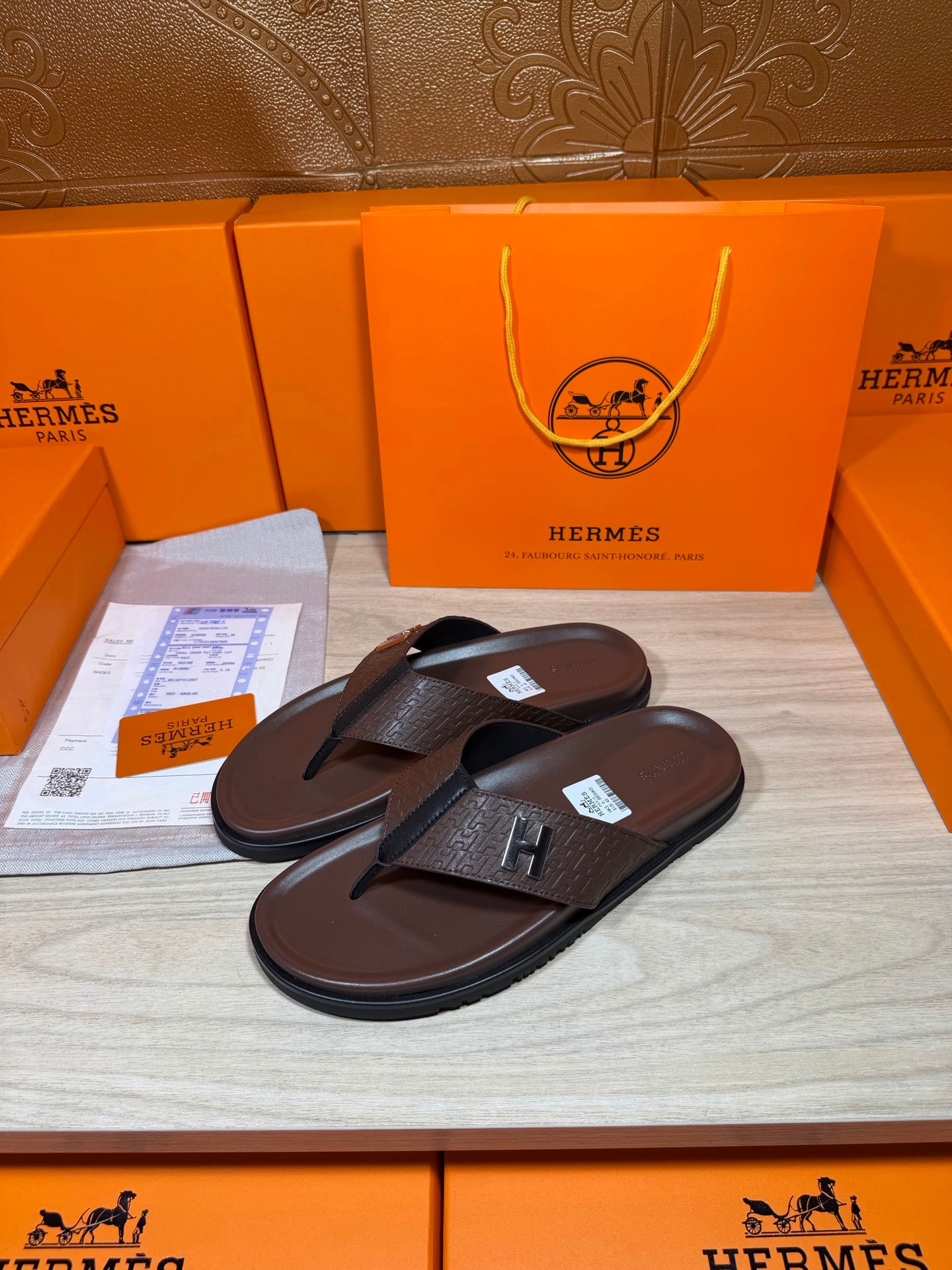 Brown leather flip-flop sandals with dark H strap detail, pair on display