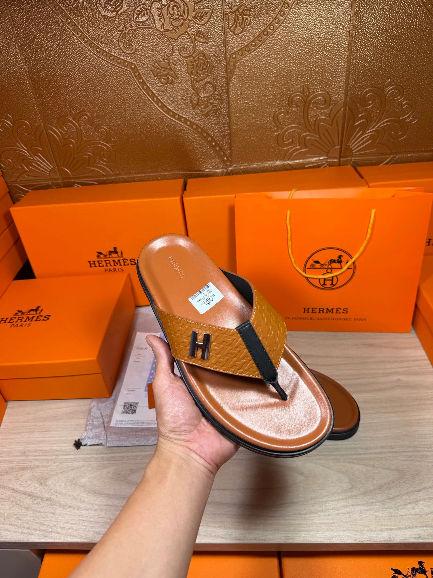 Hermes thong sandal being held, brown footbed with blue strap and H logo