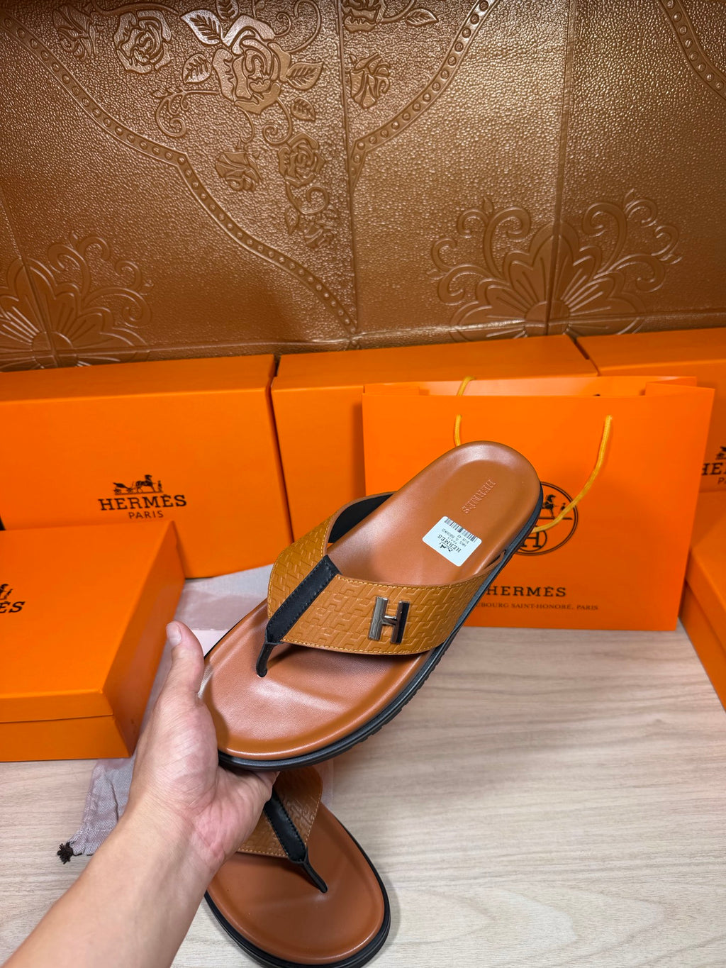 Hermes thong sandal held in hand, brown footbed with blue strap and H logo