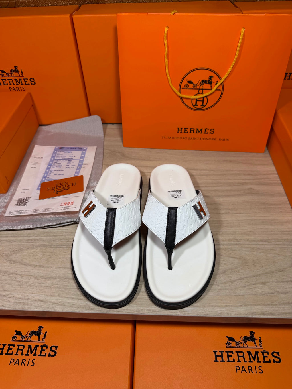 White thong sandals with black straps and H logo, pair laid on display tray