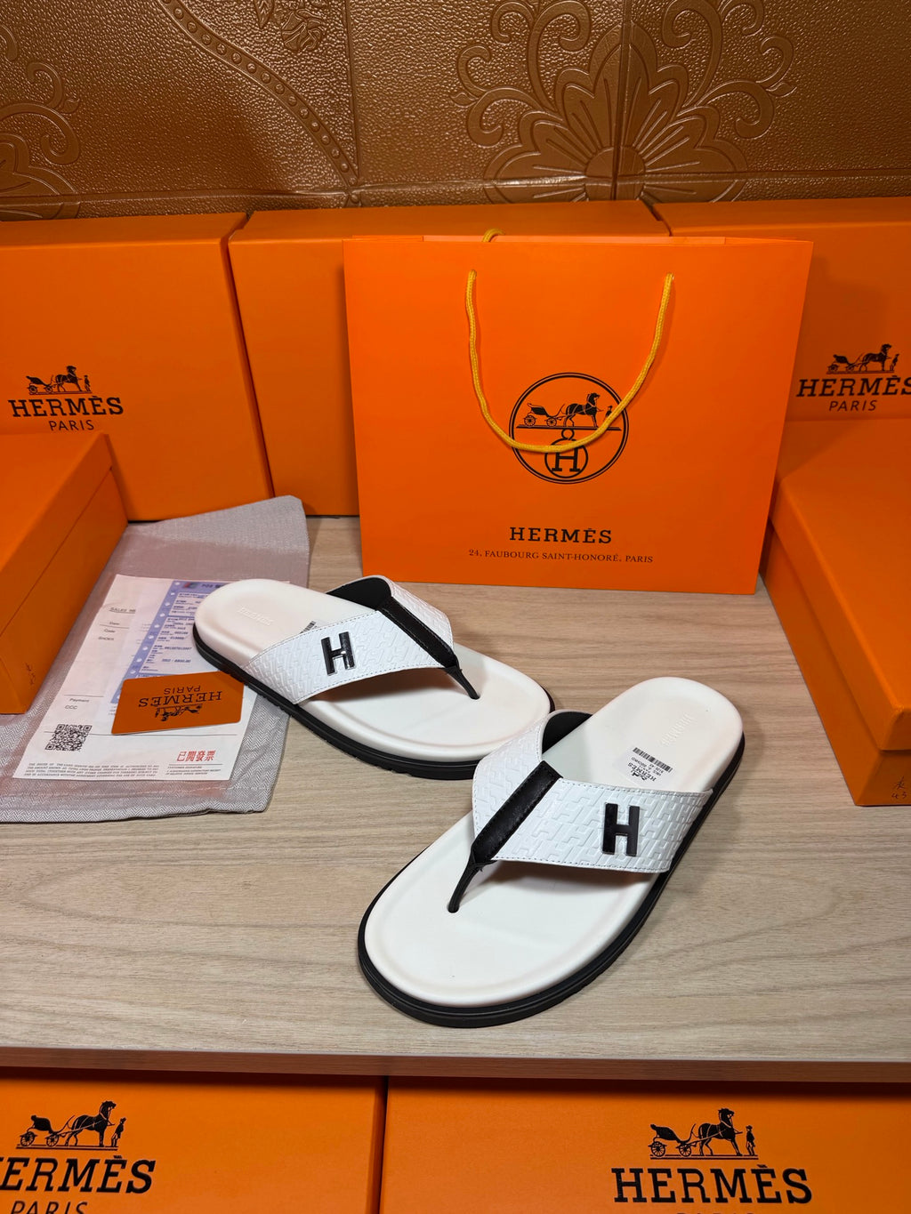 White thong sandals with black strap and H logo, one pair on display tray