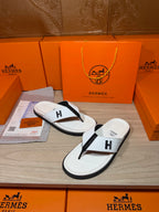 White thong sandals with black strap and H logo, one pair on display tray