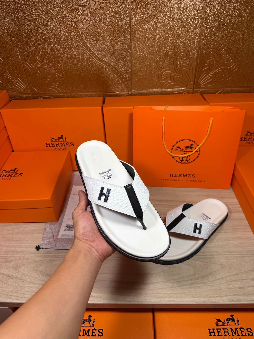 White thong sandals in hand, black strap with H logo, with orange gift box