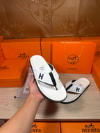 White thong sandals in hand, black strap with H logo, with orange gift box