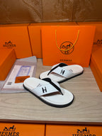 White thong sandals with black straps and H logo, shown with box and papers