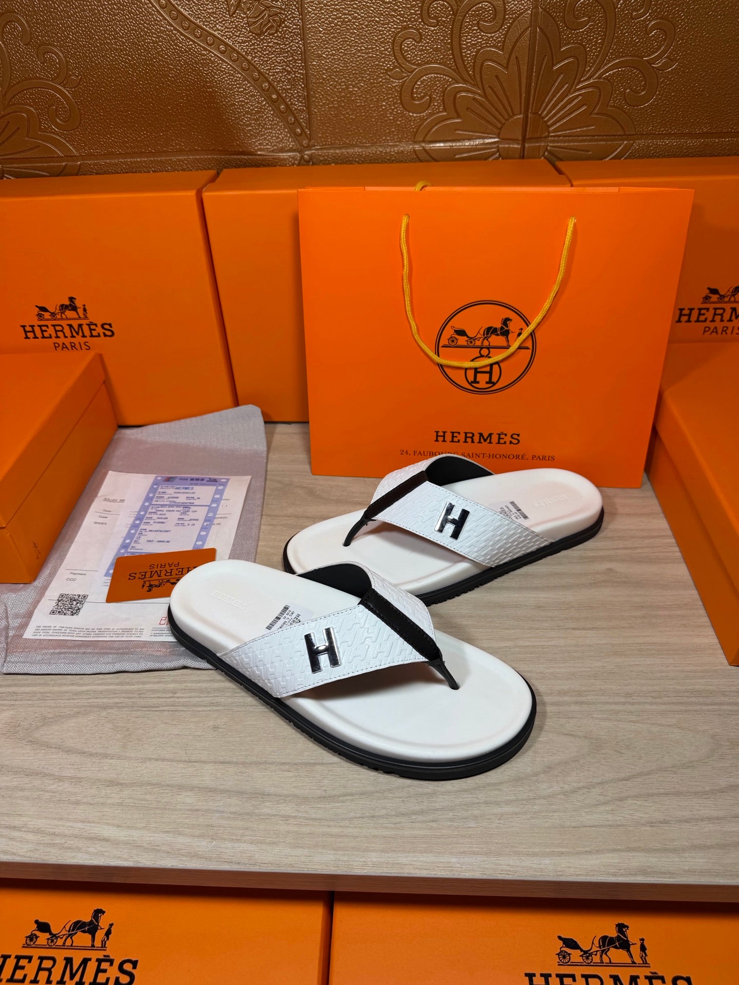 White thong sandals with black straps and H logo, shown with box and papers