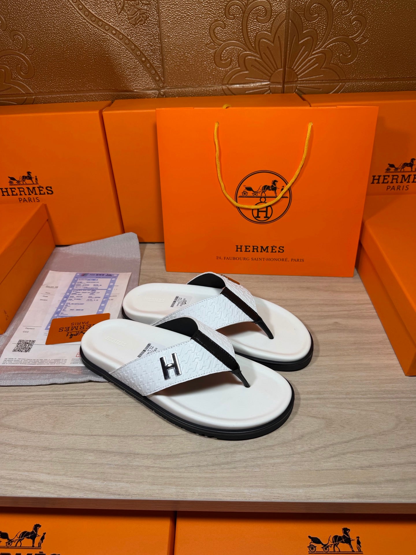 White thong sandals with black toe strap and H logo, pair on display tray