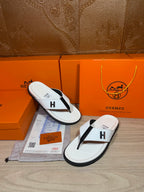 White thong sandals with black straps and H logo, side view on display tray