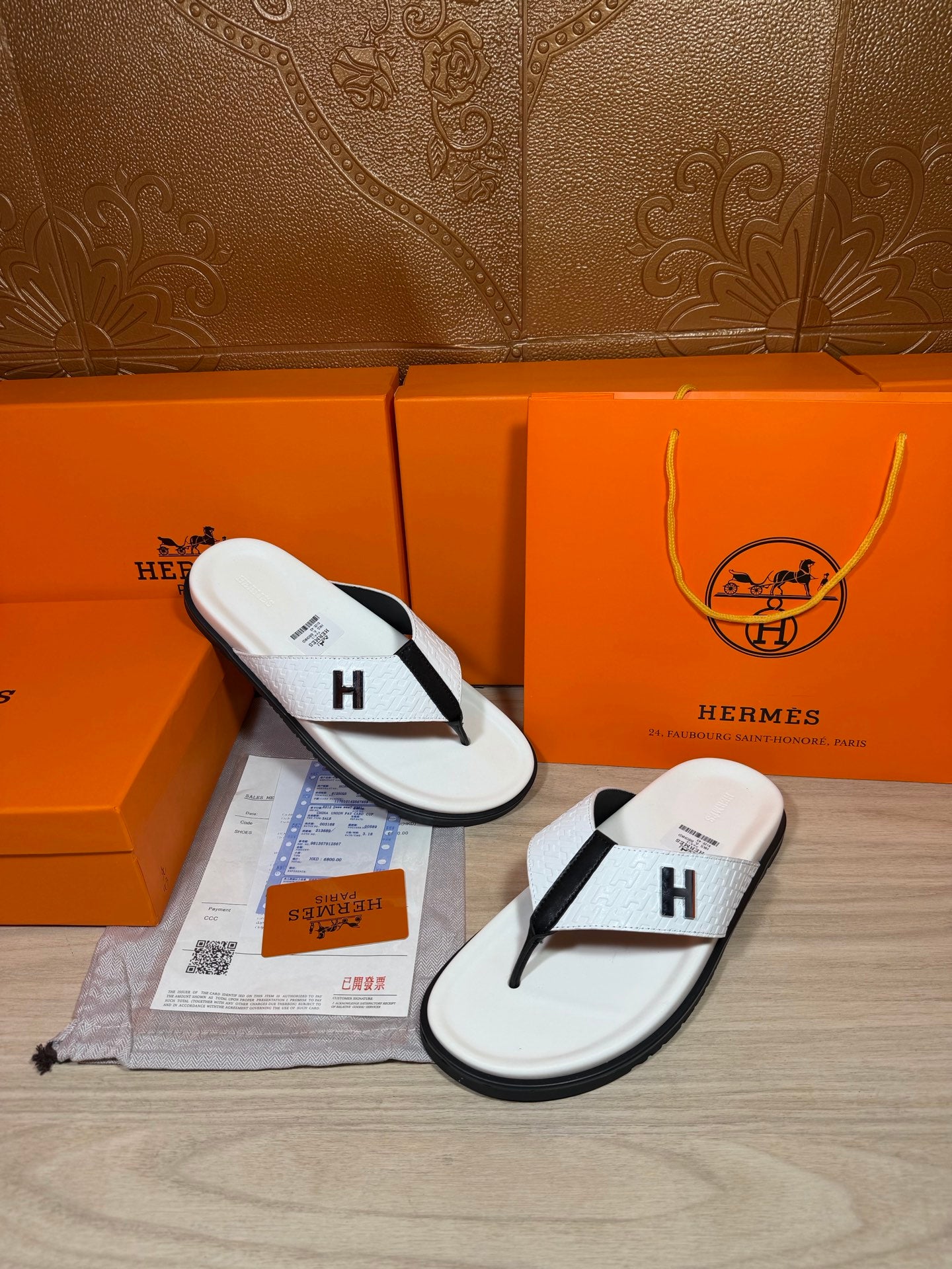 White thong sandals with black straps and H logo, side view on display tray