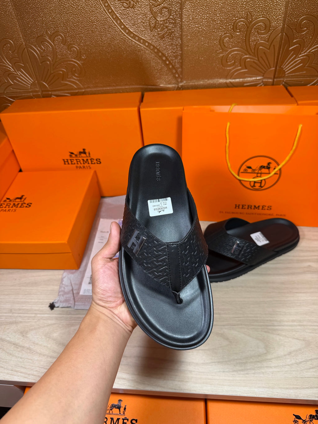 Black leather slide sandals held by hand, one with H logo strap visible