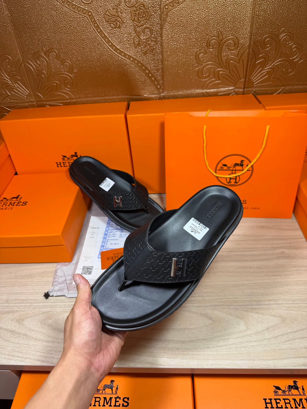 Black leather slide sandals held up, showing H logo strap and textured finish
