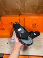 Black leather slide sandal held in hand, showing H logo strap and flat sole