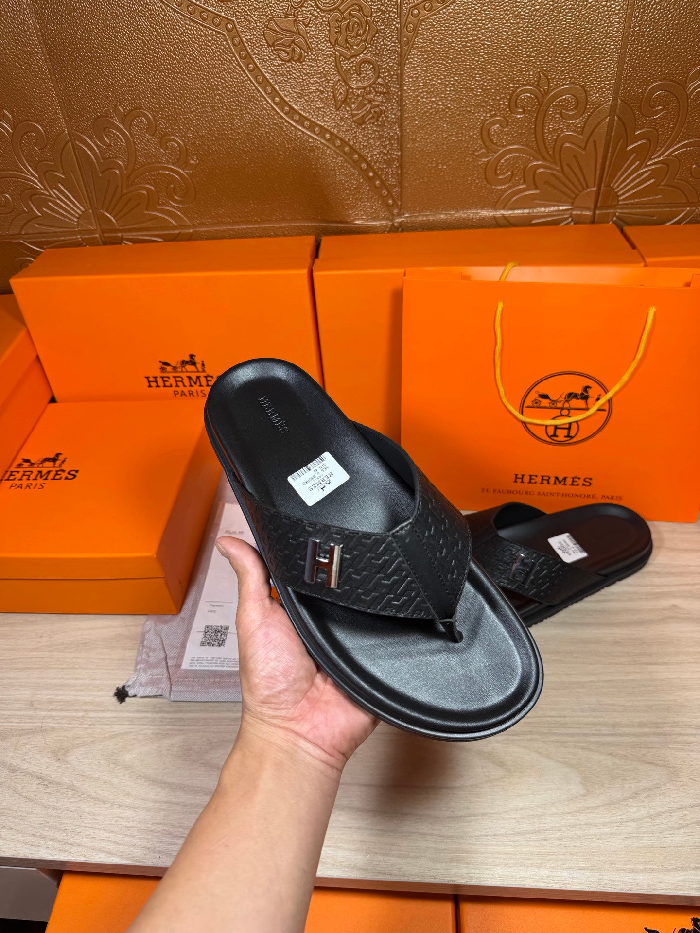 Black leather slide sandal held in hand, showing H logo strap and flat sole