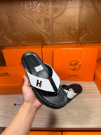 Hermes leather sandals held in hand, black and white thong style with H logo.