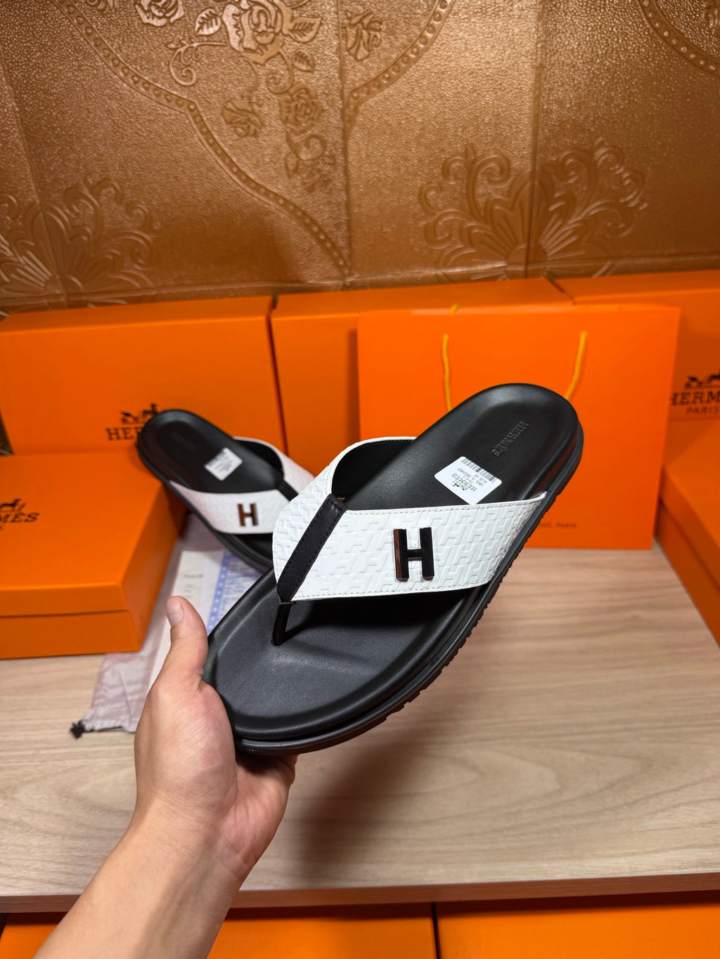 Hermes sandals held up: black sole and straps with white panel and H logo.