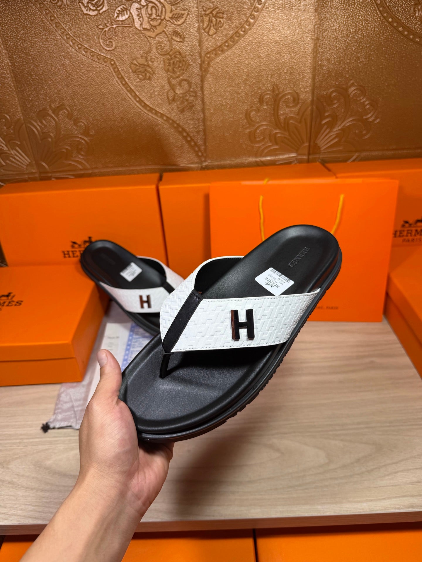 Hermes sandals held up: black sole and straps with white panel and H logo.