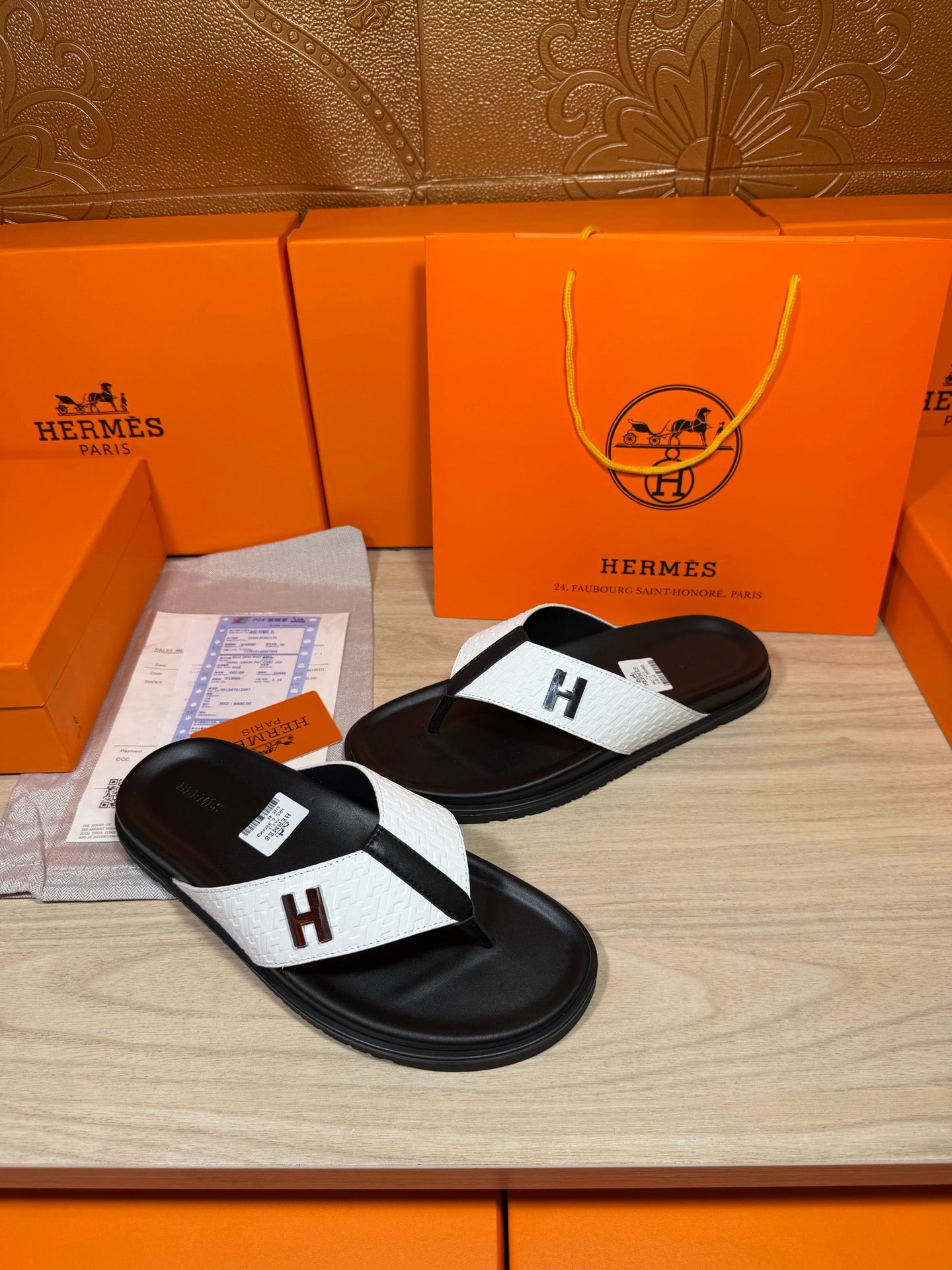 Hermes flat thong sandals with black sole, white strap panel, and H logo buckle.