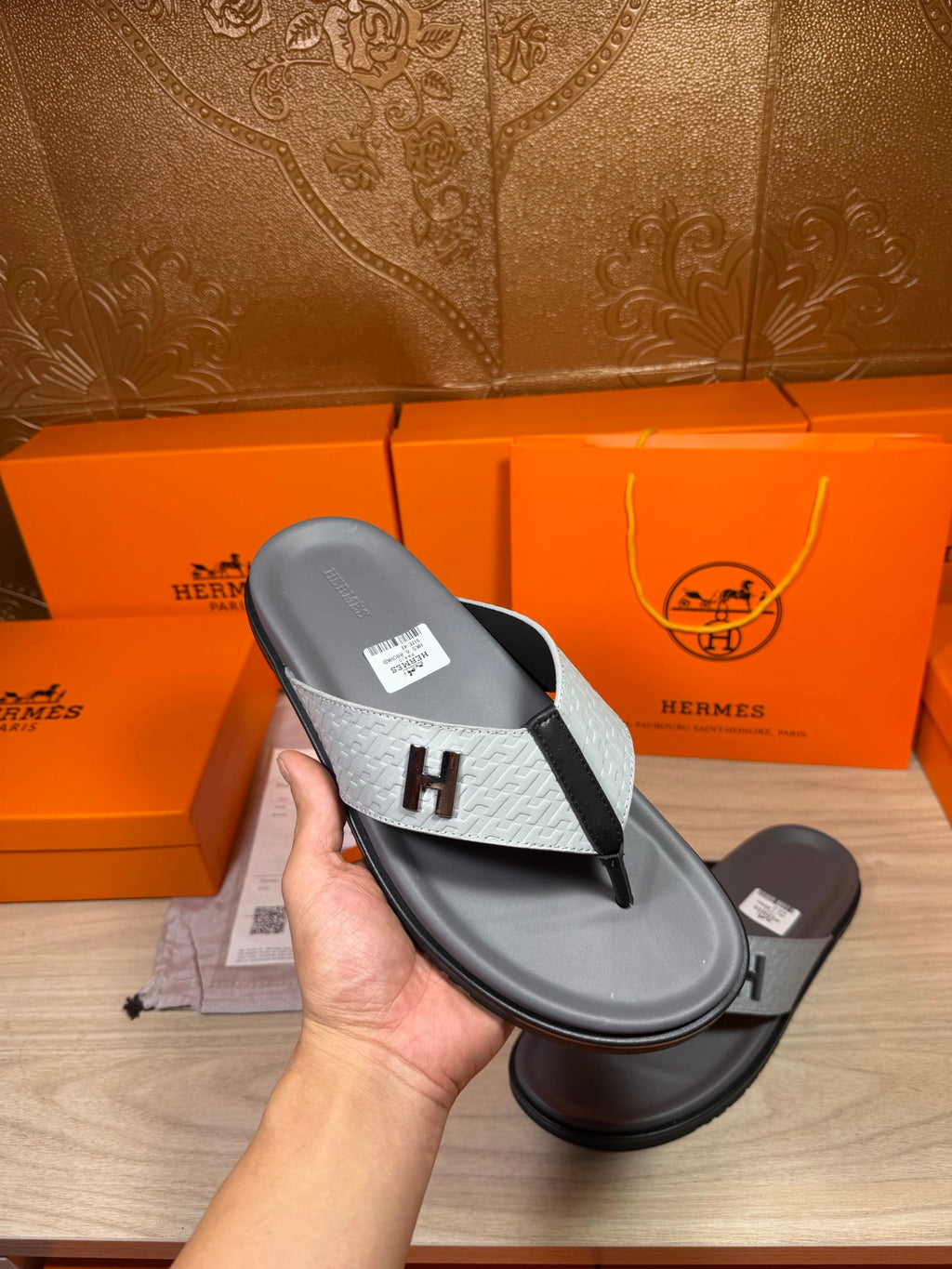 Hermes thong sandal held in hand, dark gray sole with gray H logo strap
