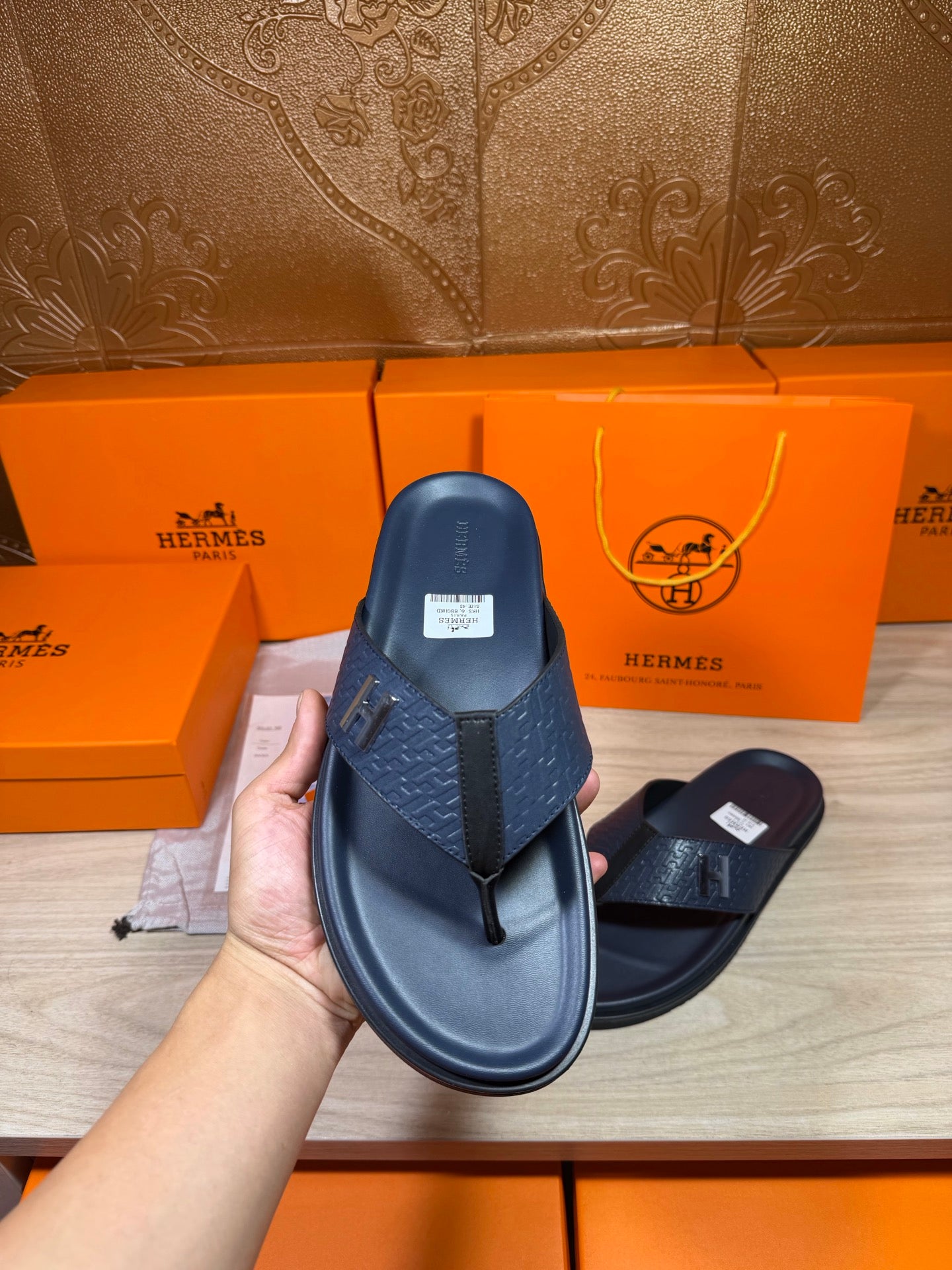 Hermes leather sandals in dark blue held for display, front strap with H emblem