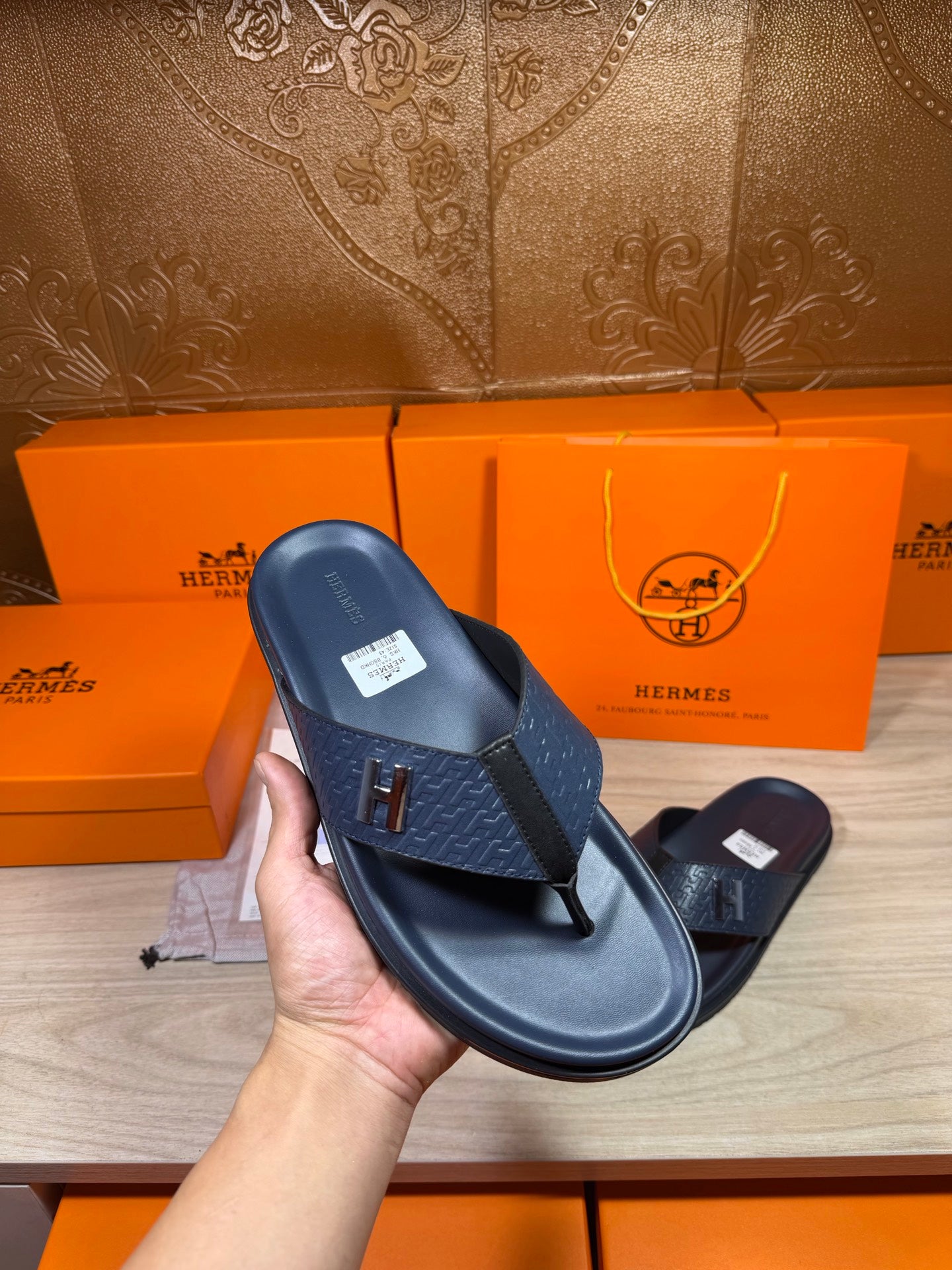 Hermes leather sandal in dark blue, close-up held in hand with H logo on strap