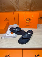 Hermes leather flip-flops in dark blue, one sandal foreground with H emblem on strap