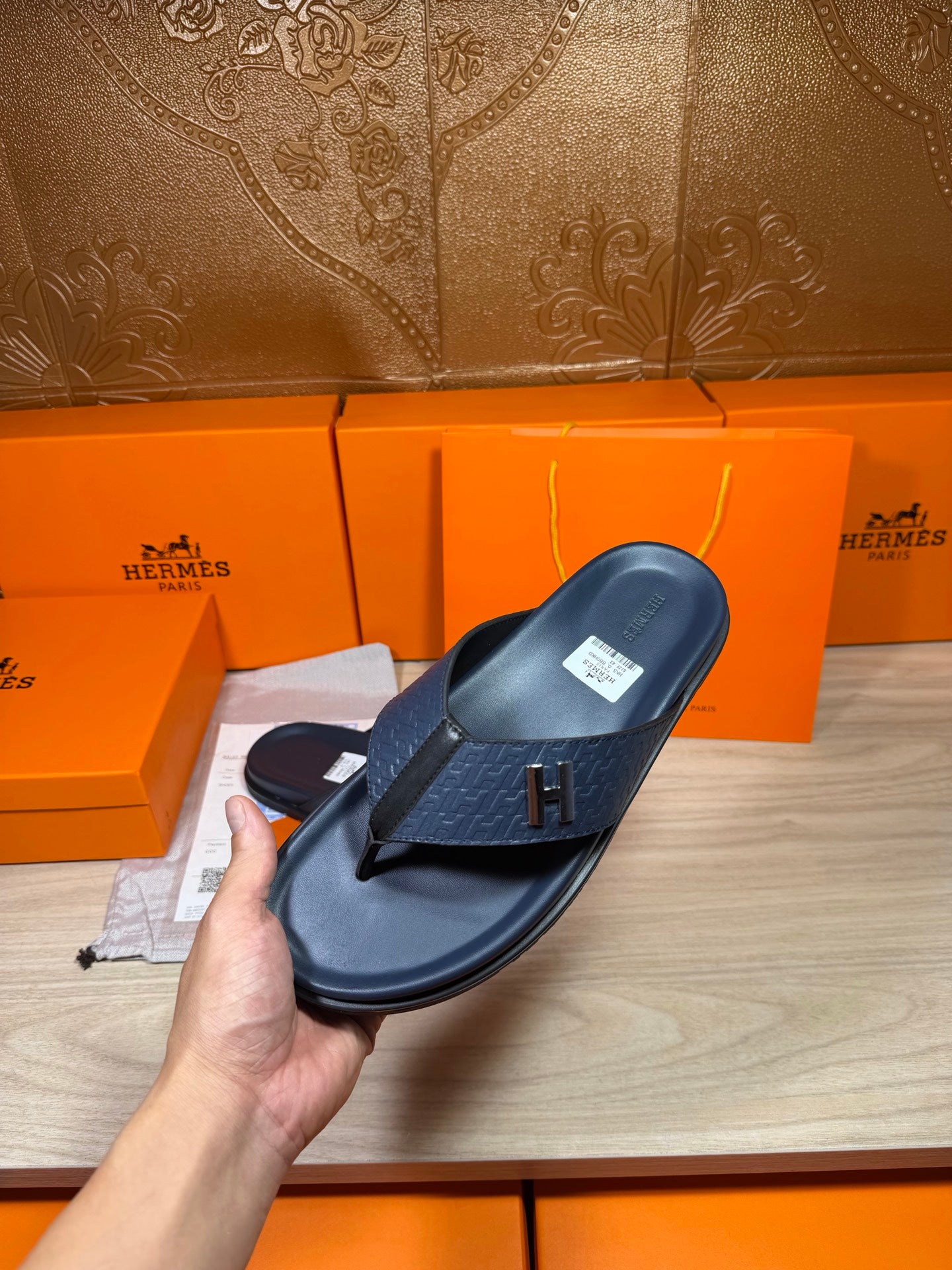 Hermes leather sandal in dark blue held by hand, textured strap and H emblem detail