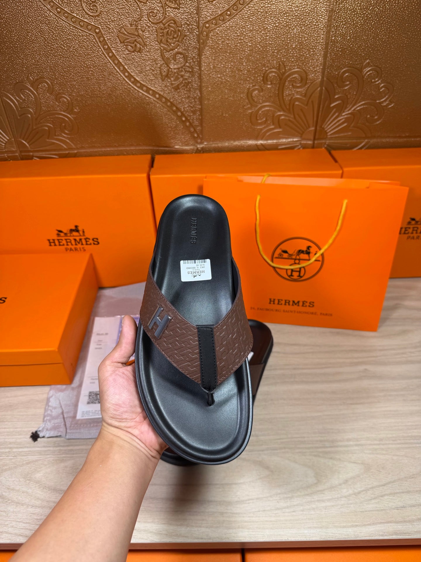 Single brown-and-black H-logo thong sandal held up, showing footbed and strap