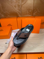 Single black-and-brown H-logo thong sandal held in hand, side profile view