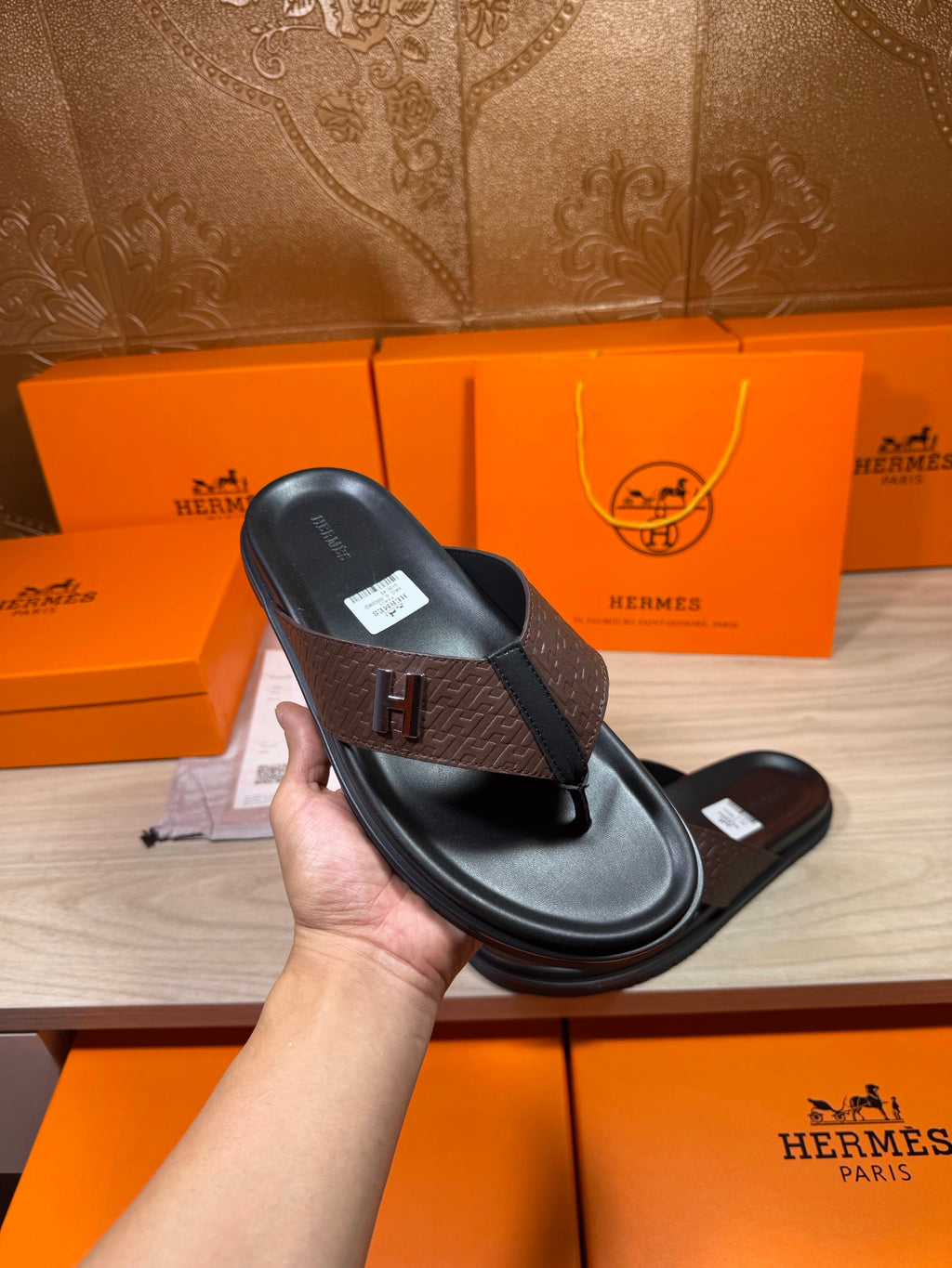 Single black-and-brown H-logo thong sandal held in hand, showing top view
