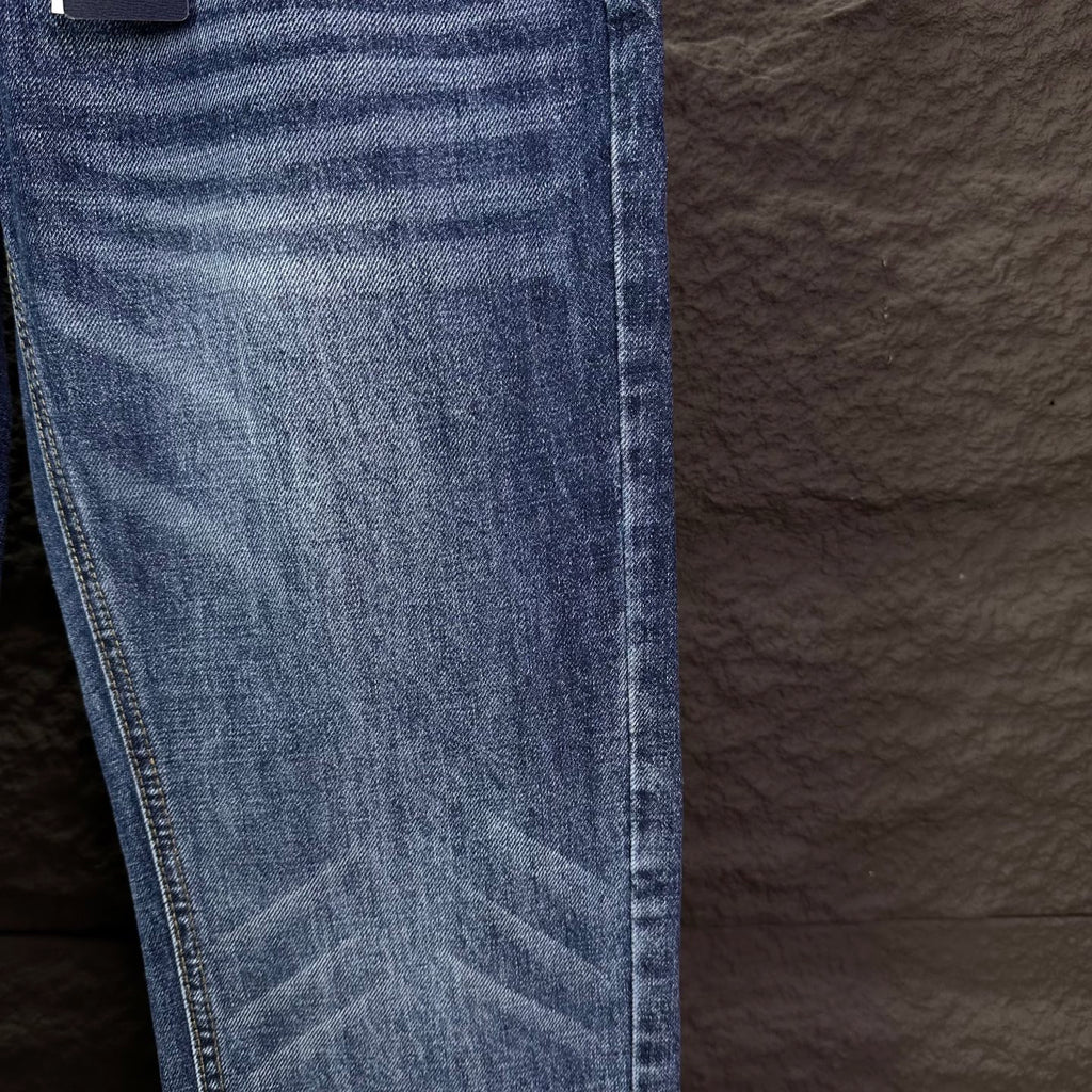 Blue denim jeans leg close-up with whiskering and stitched hem.