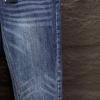 Blue denim jeans leg close-up with whiskering and stitched hem.