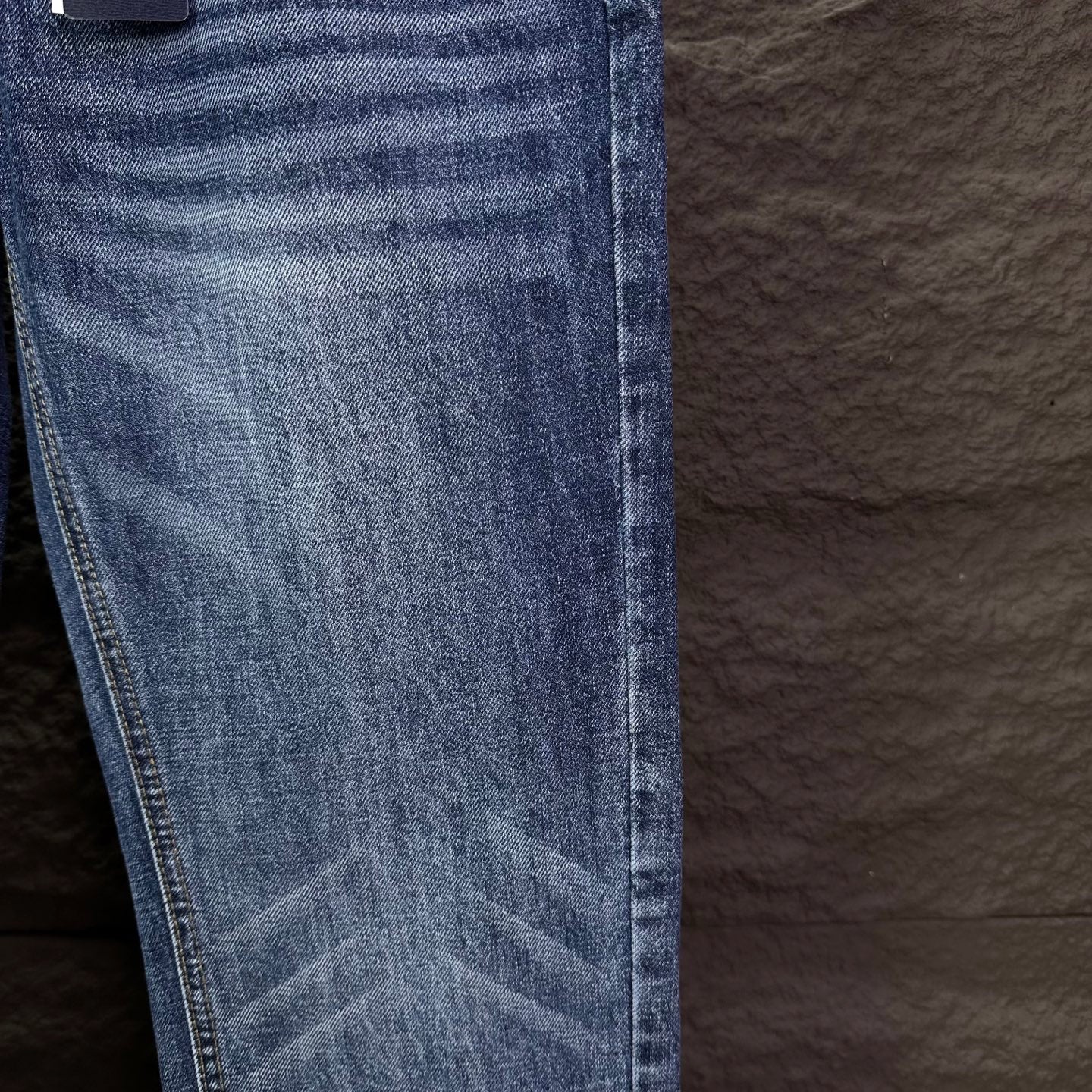 Blue denim jeans leg close-up with whiskering and stitched hem.